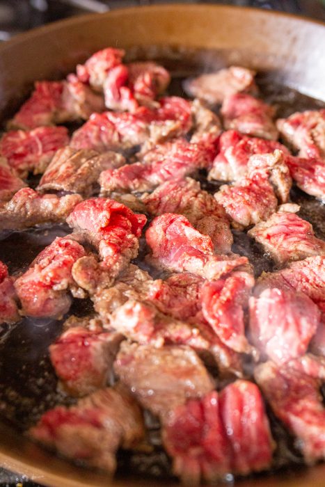 Raw beef pieces being cooked in a skillet.