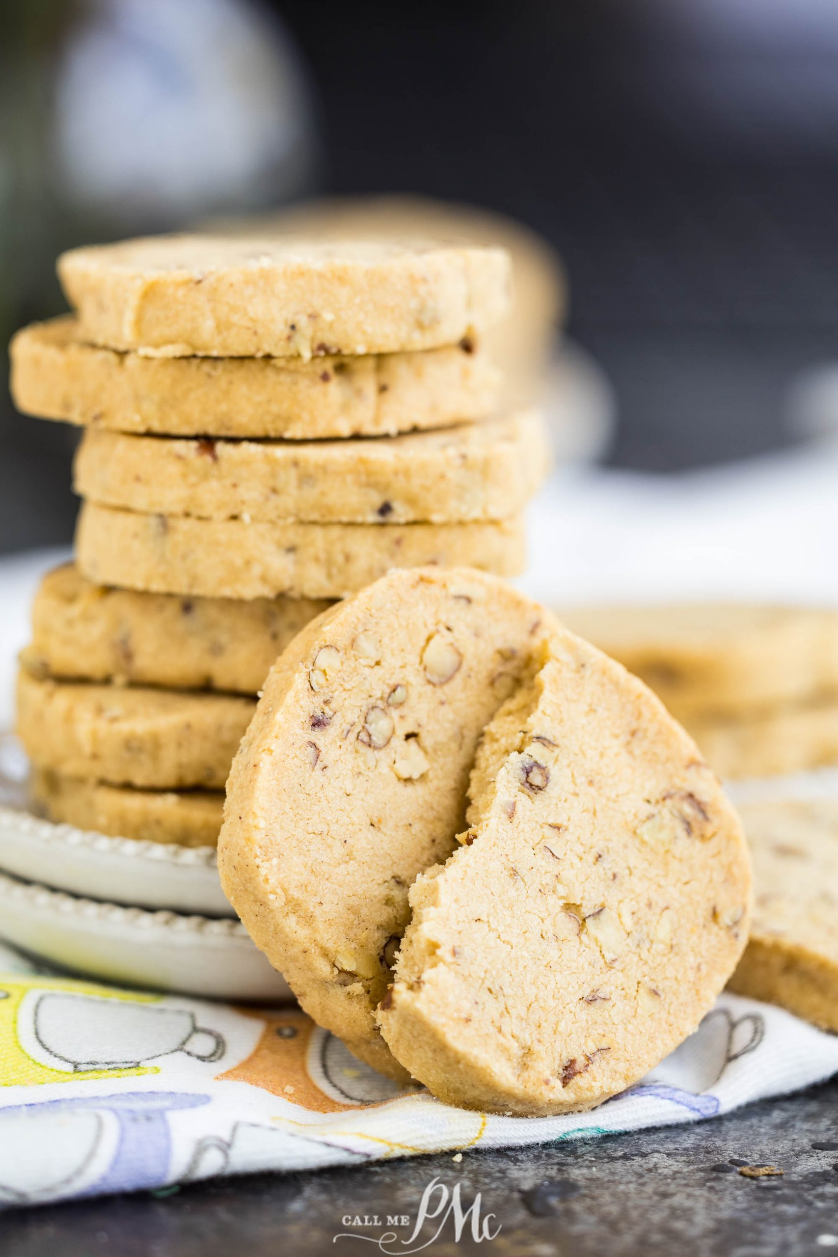 A stack of round cookies on a plate with one cookie broken in half in the foreground.