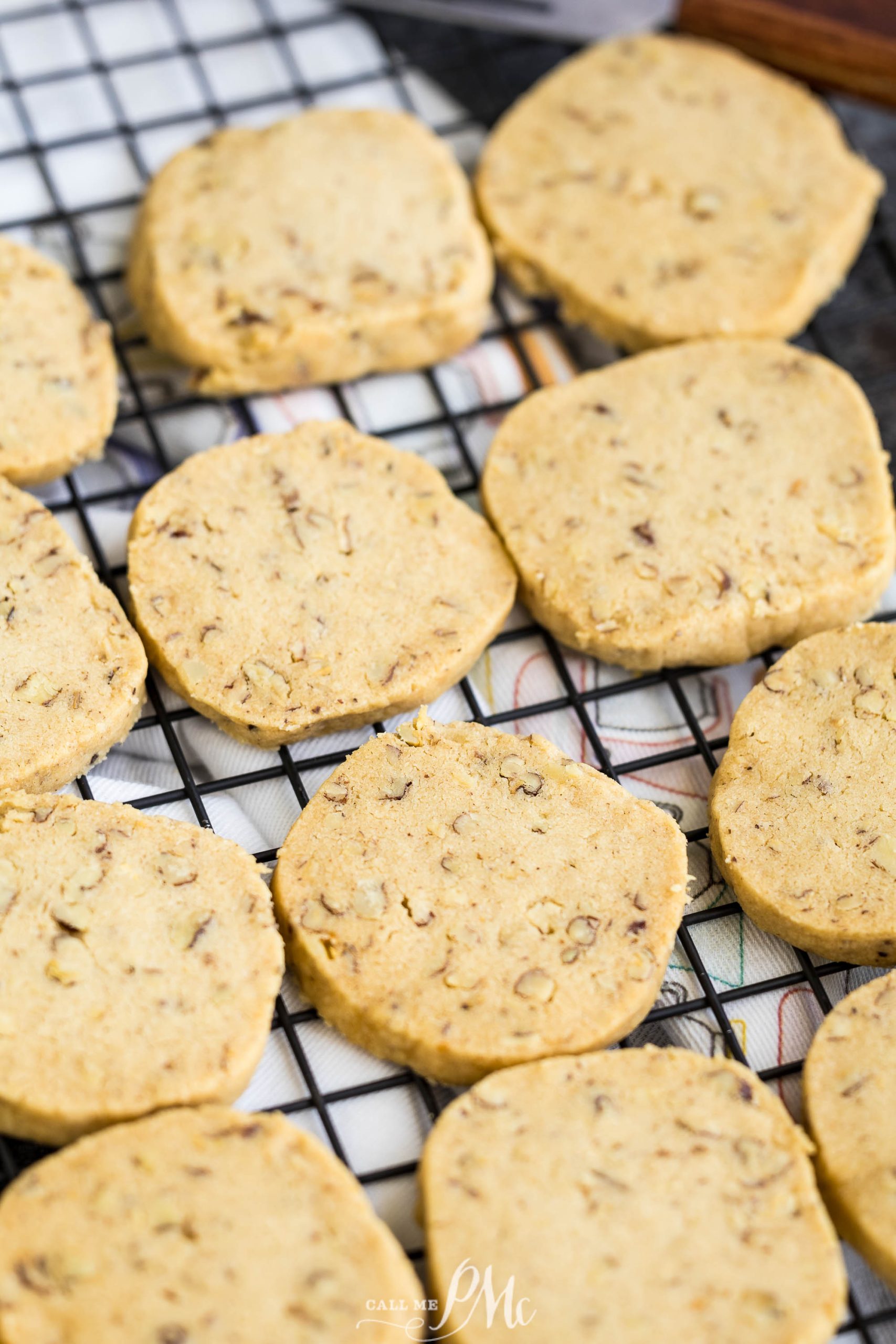 Round, textured cookies with visible nut pieces cooling on a black wire rack over a checkered cloth.