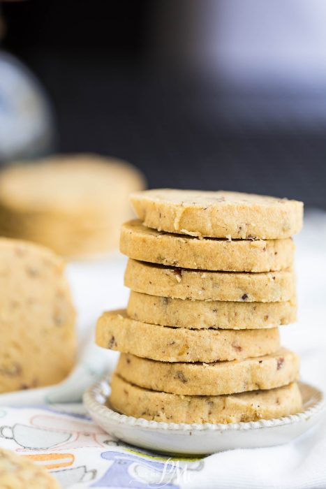 A stack of round, beige cookies with visible nuts on a small plate, with a blurred background.