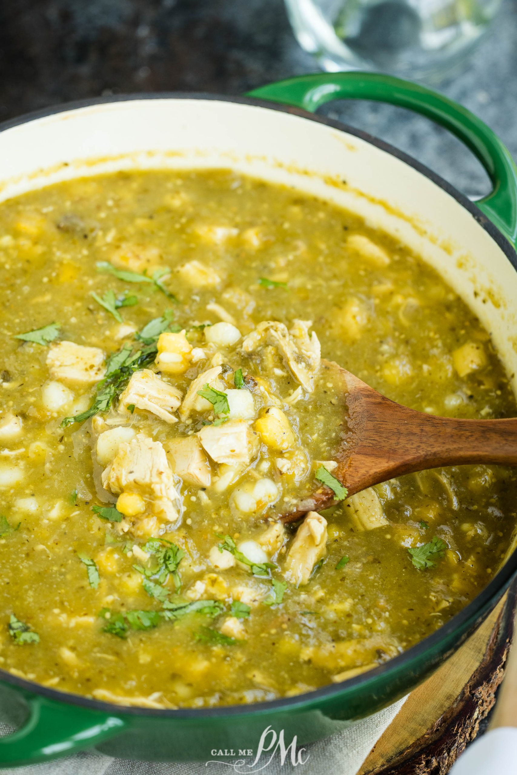 A pot of green chili chicken stew with chunks of chicken, hominy, and herbs.