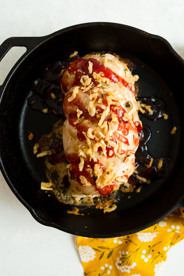 A cooked meatloaf in a cast iron skillet topped with sauce and crispy fried onions.