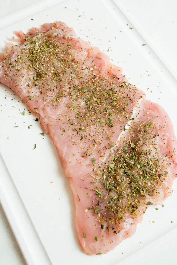 Raw turkey breast seasoned with herbs and spices on a white cutting board.