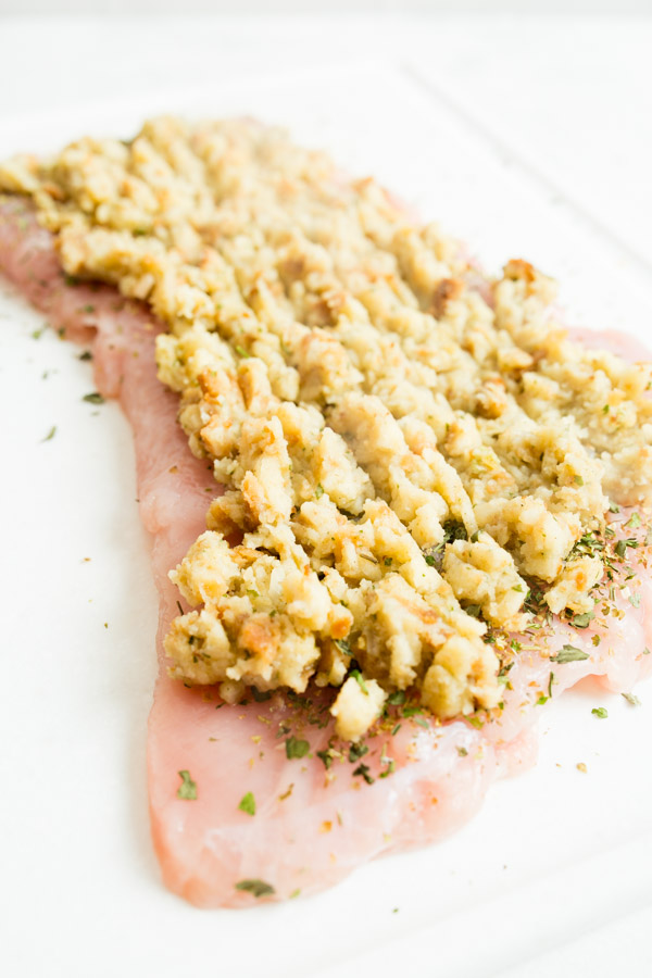 Raw chicken breast topped with a layer of stuffing on a white surface.