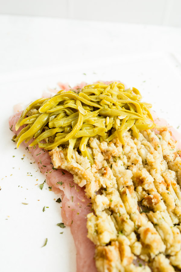 Raw turkey breast topped with stuffing and green beans on a white surface.