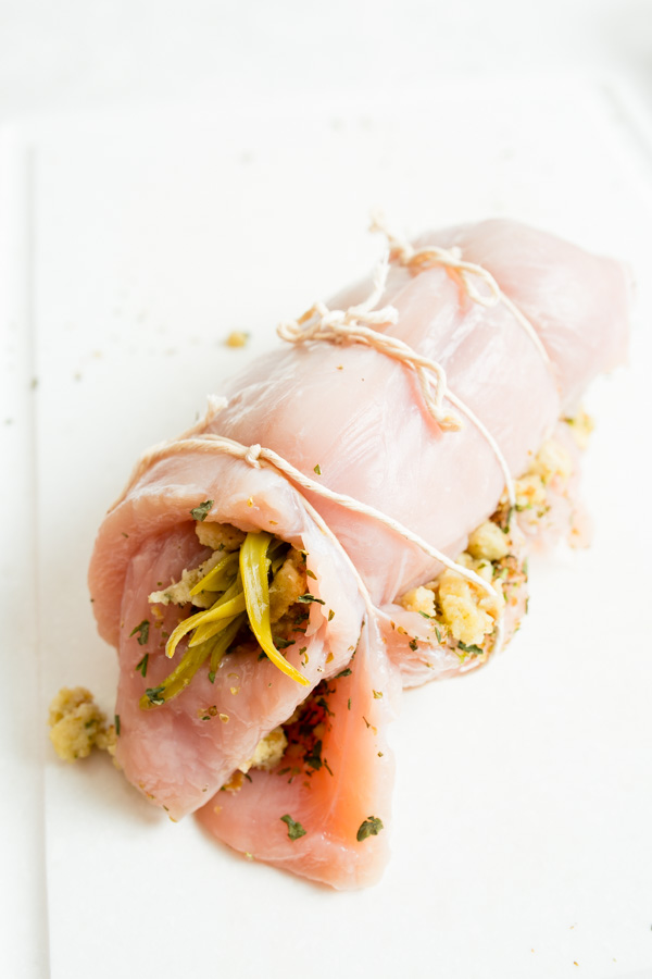 Raw chicken breast rolled and tied with string, stuffed with herbs, breadcrumbs, and sliced vegetables.