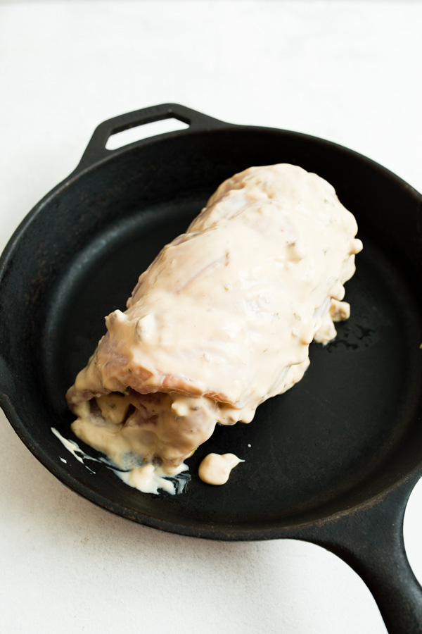 Chicken breast coated in a creamy white sauce on a black skillet.