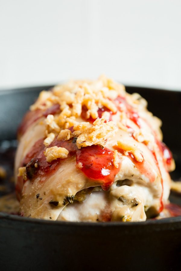 A cooked chicken breast topped with a glaze, garnish, and crispy onions in a black skillet.