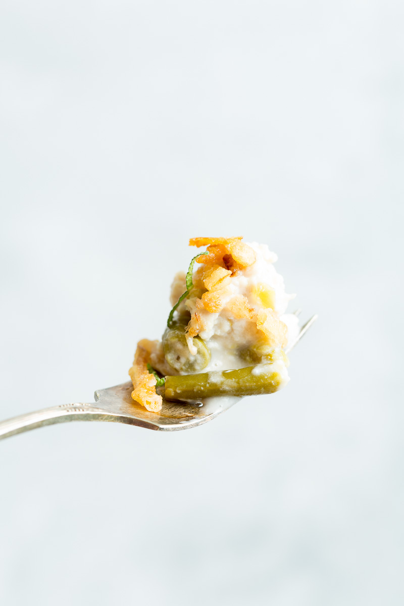 A fork holds a bite of green bean casserole topped with fried onions against a light background.