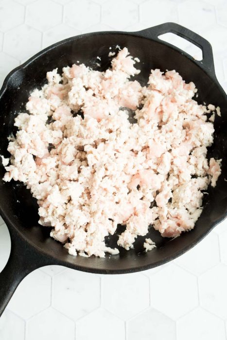 Ground turkey cooking in a black cast iron skillet on a white hexagonal tile surface.