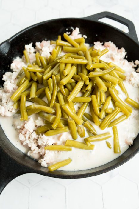 A skillet contains green beans on top of ground meat in a white sauce.