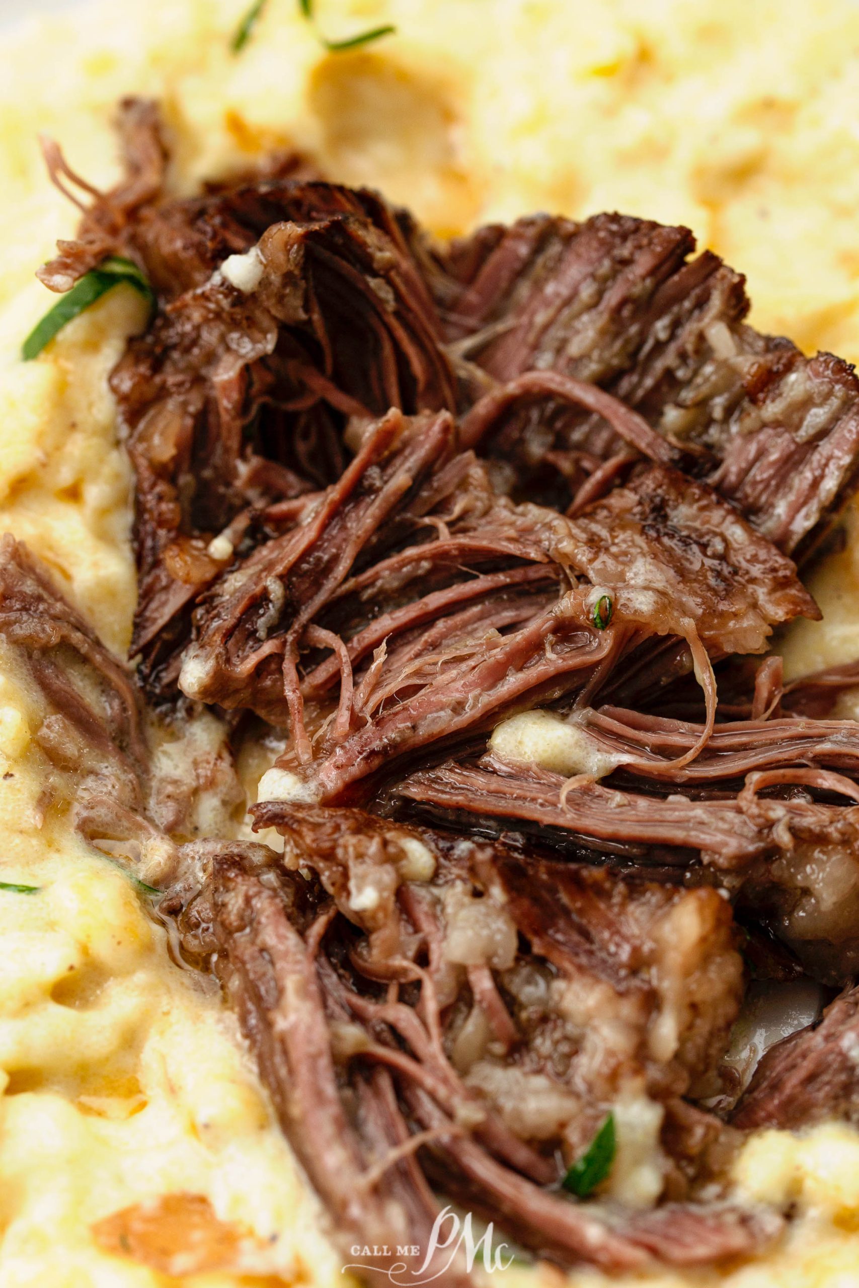 Close-up of tender shredded beef served over creamy mashed potatoes, garnished with fresh herbs.