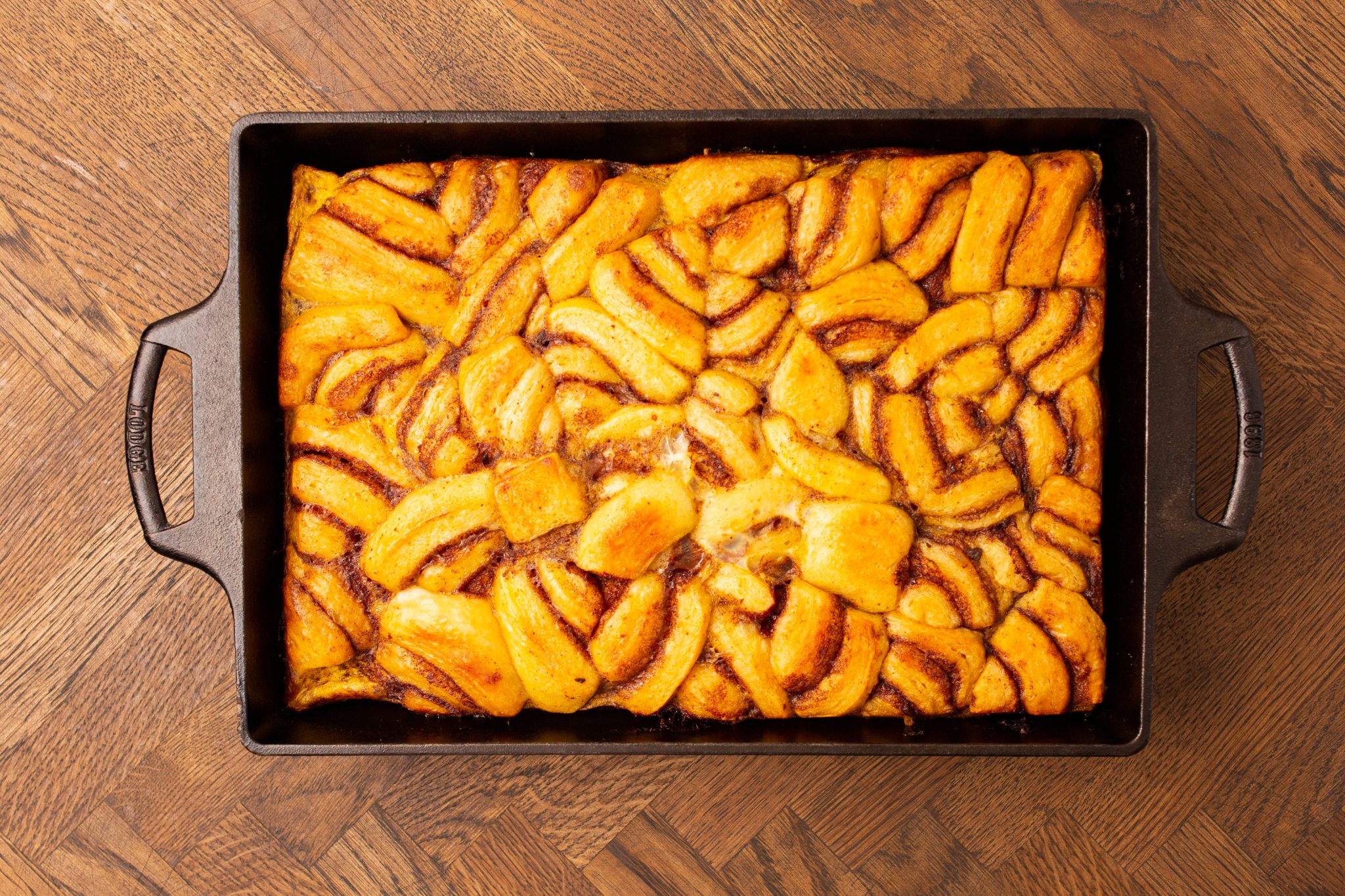 A rectangular baking dish filled with baked cinnamon rolls, arranged closely together, on a wooden surface.