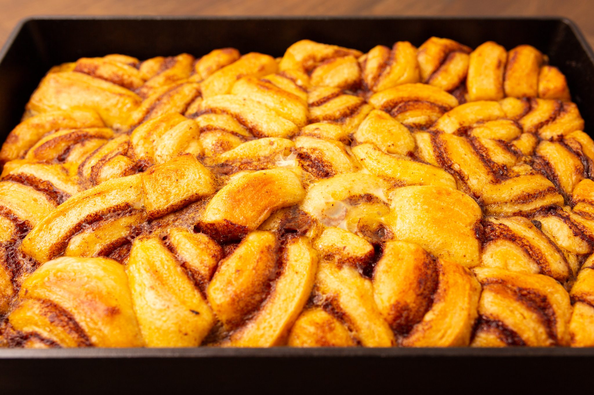 Freshly baked bread in a black baking tray, with golden brown swirls and a glazed finish.