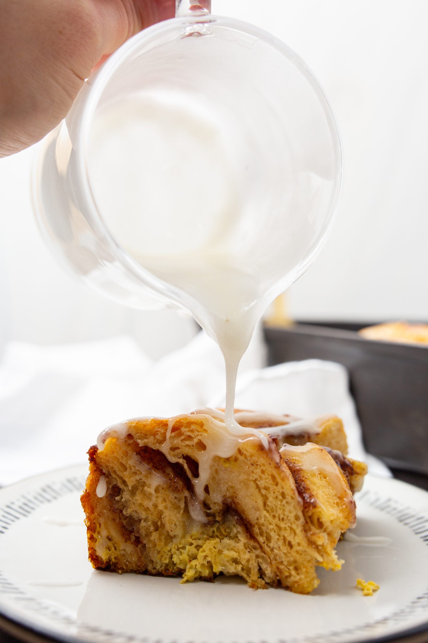 Icing being poured over a cinnamon roll slice on a plate.