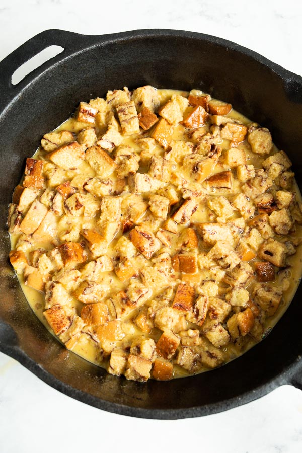 A skillet filled with cubed bread soaked in a mixture, ready for baking.