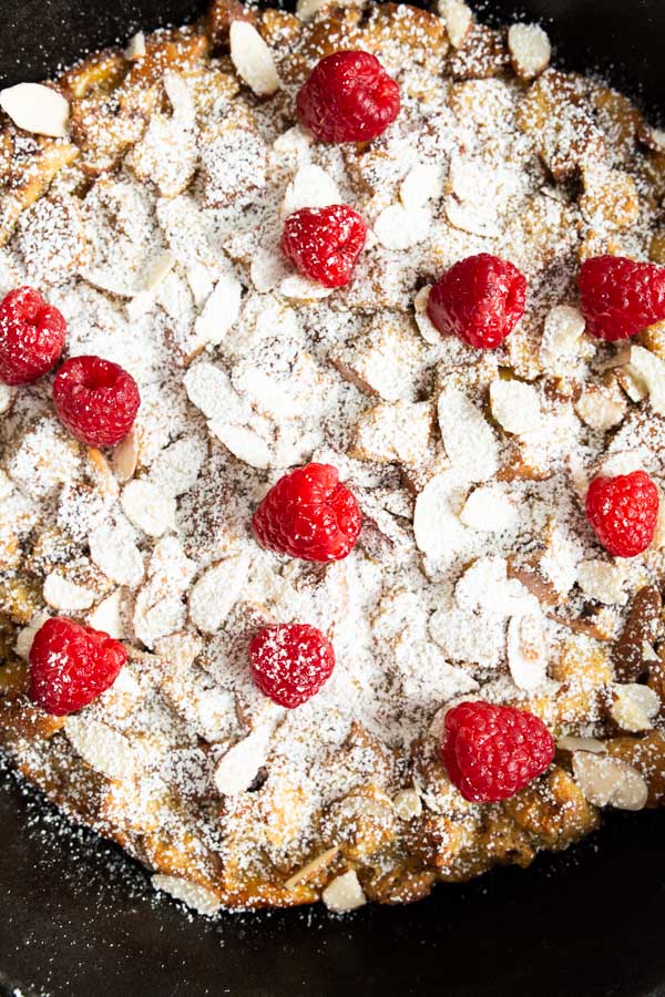 A dessert topped with sliced almonds, powdered sugar, and evenly spaced raspberries.