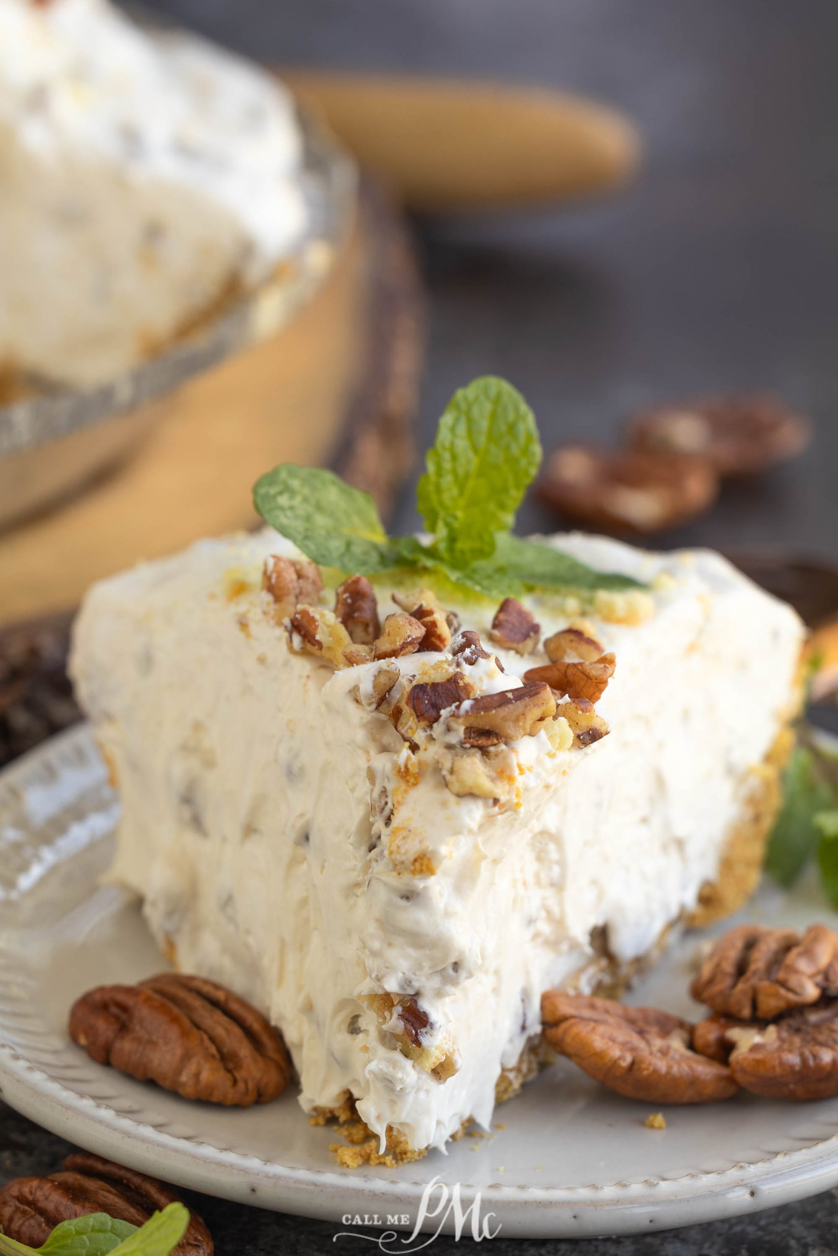 A slice of cream pie with pecans on a plate, garnished with a mint leaf, surrounded by pecans.