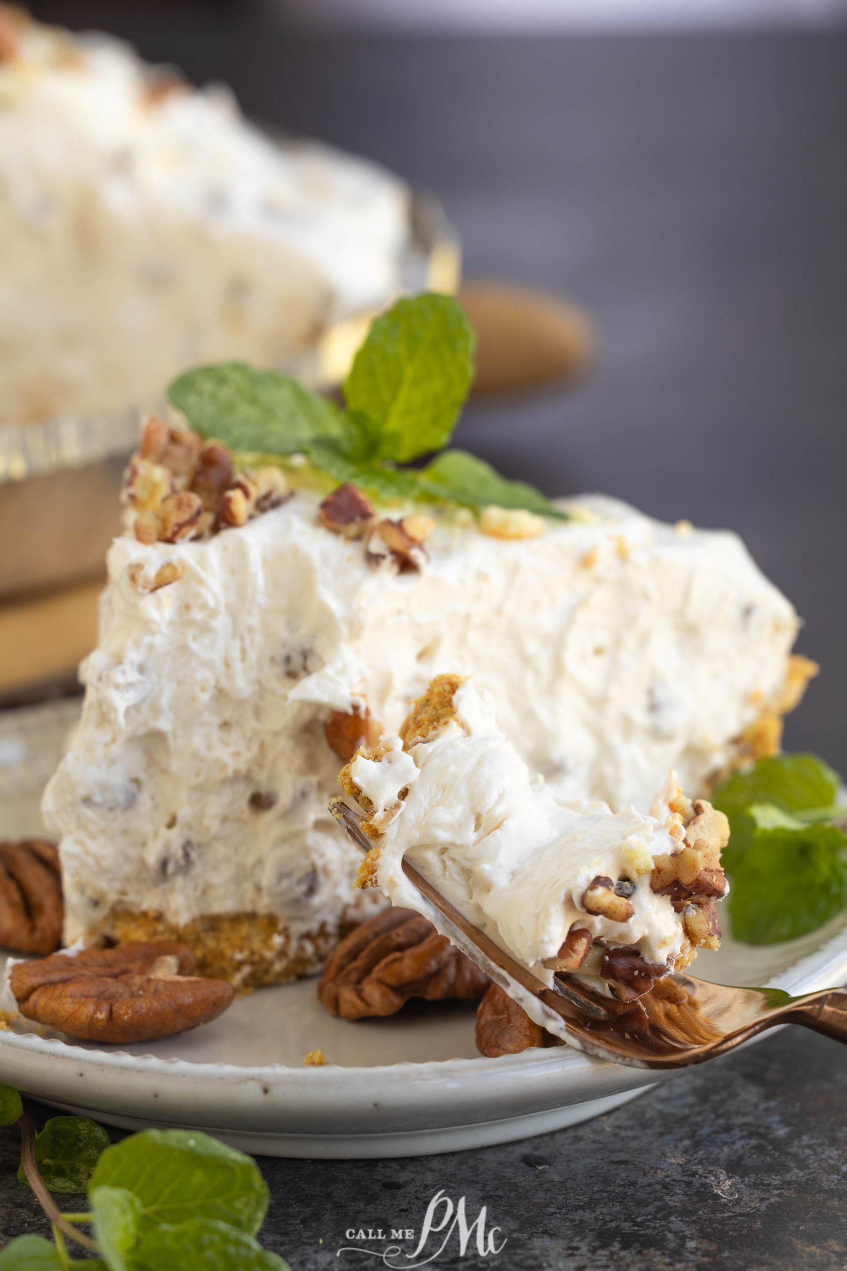 A slice of creamy white pie with a nutty topping sits on a plate, garnished with mint leaves. A fork holds a bite of the pie.