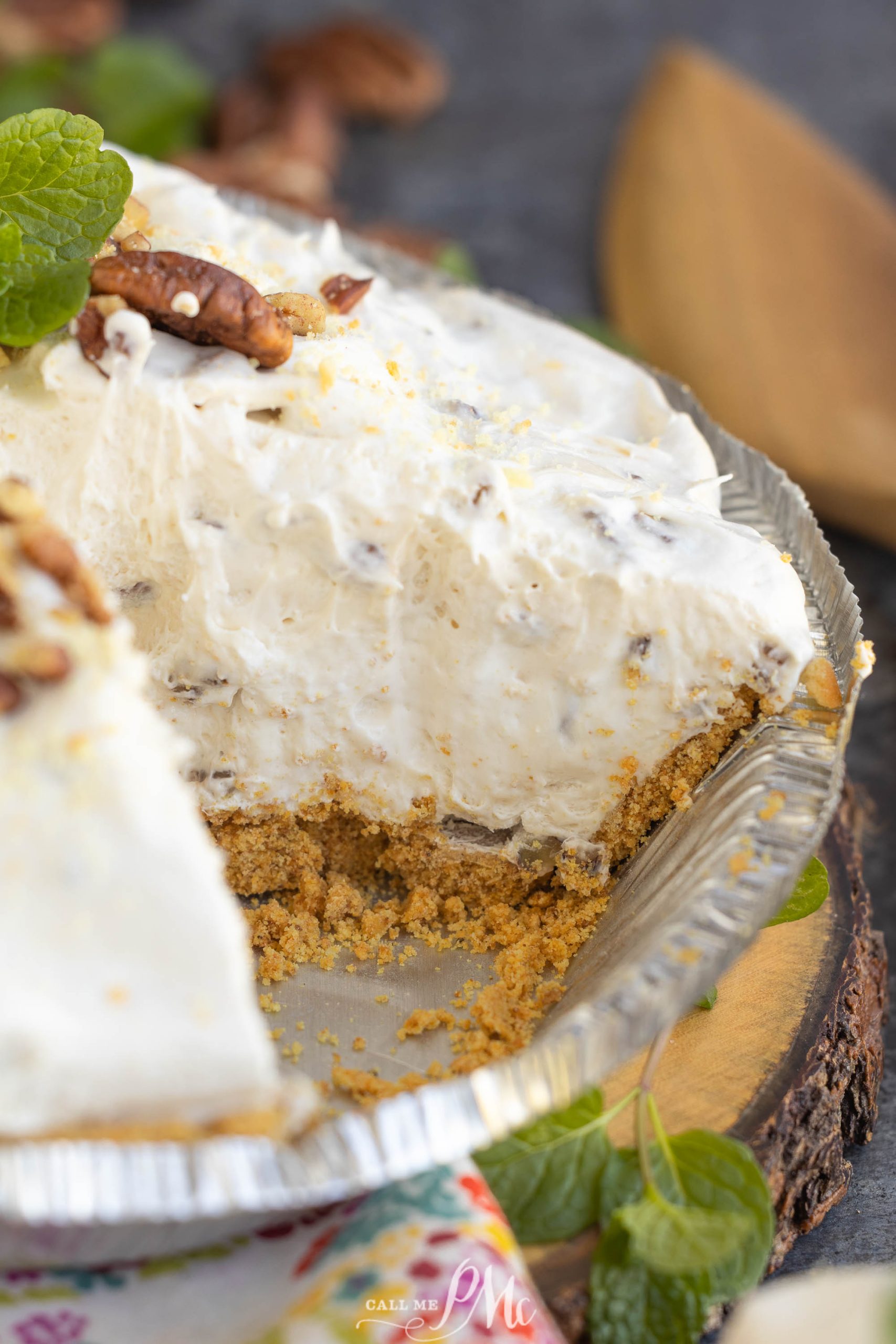 A pie with a graham cracker crust and creamy filling, partially sliced. Topped with chopped pecans and a sprig of mint.