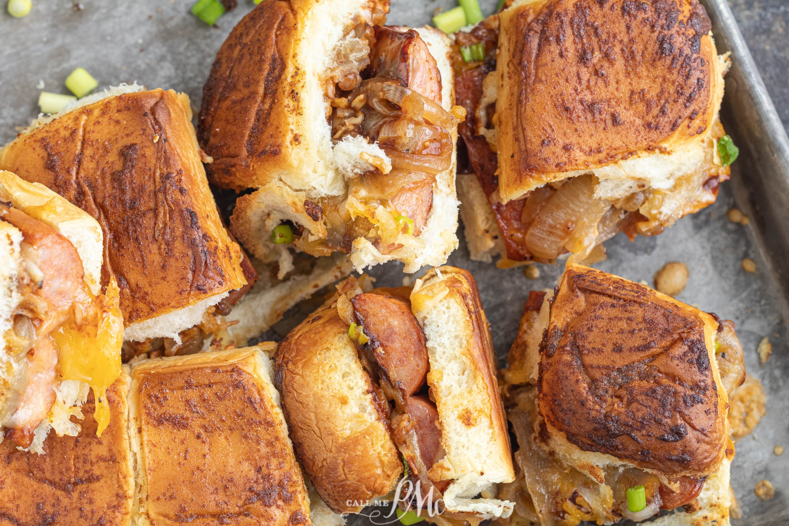 Close-up of sliced sandwiches with sausage, cheese, and caramelized onions on toasted bread, placed on a baking tray.