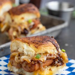 Grilled sausage with caramelized onions and peppers in a toasted roll on a blue-and-white checkered napkin.