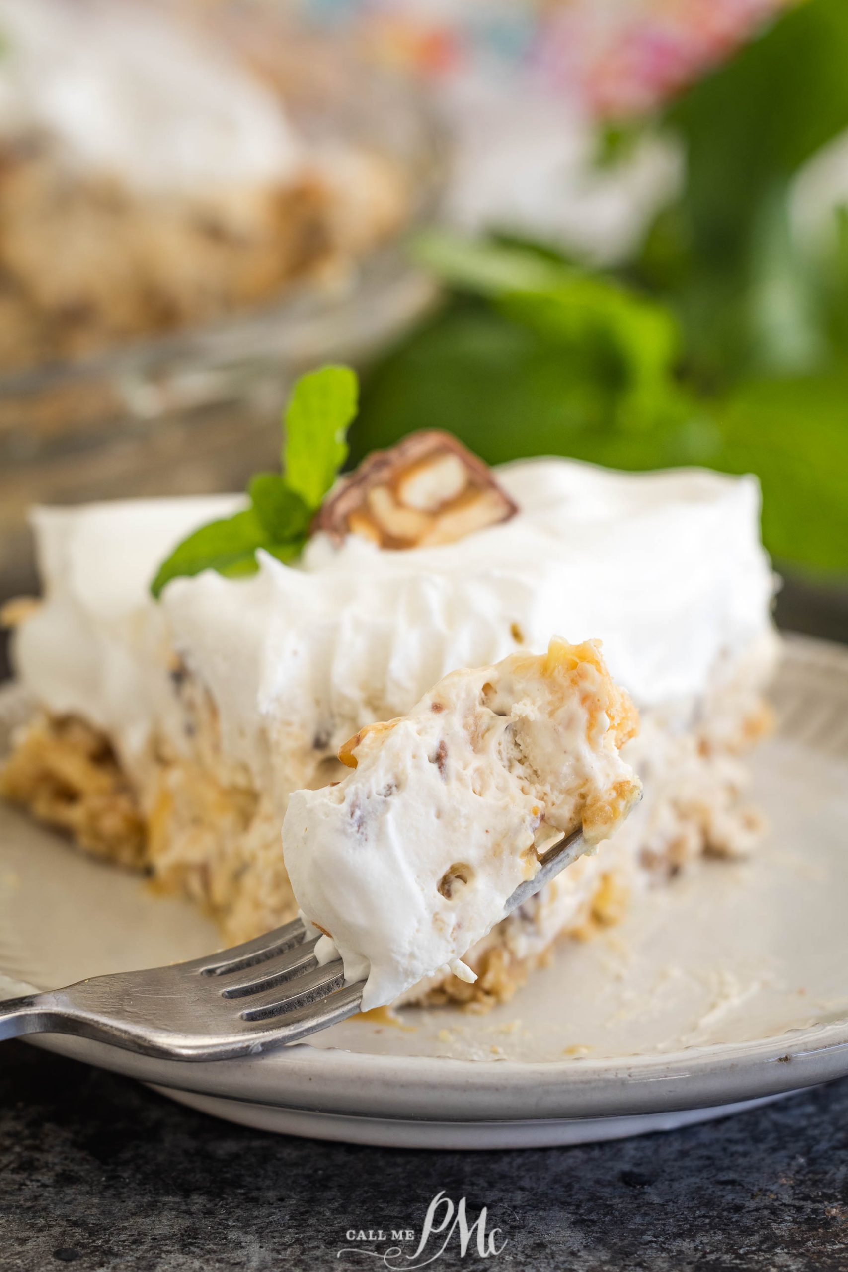 A fork holds a bite of creamy, surprise dessert topped with whipped cream and a piece of chocolate, garnished with a mint leaf, reminiscent of a million dollar pie, on a plate.