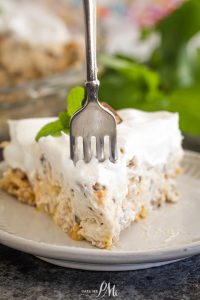 A fork is stuck into a slice of surprise million dollar pie, layered with whipped topping on a plate and garnished with a mint leaf.