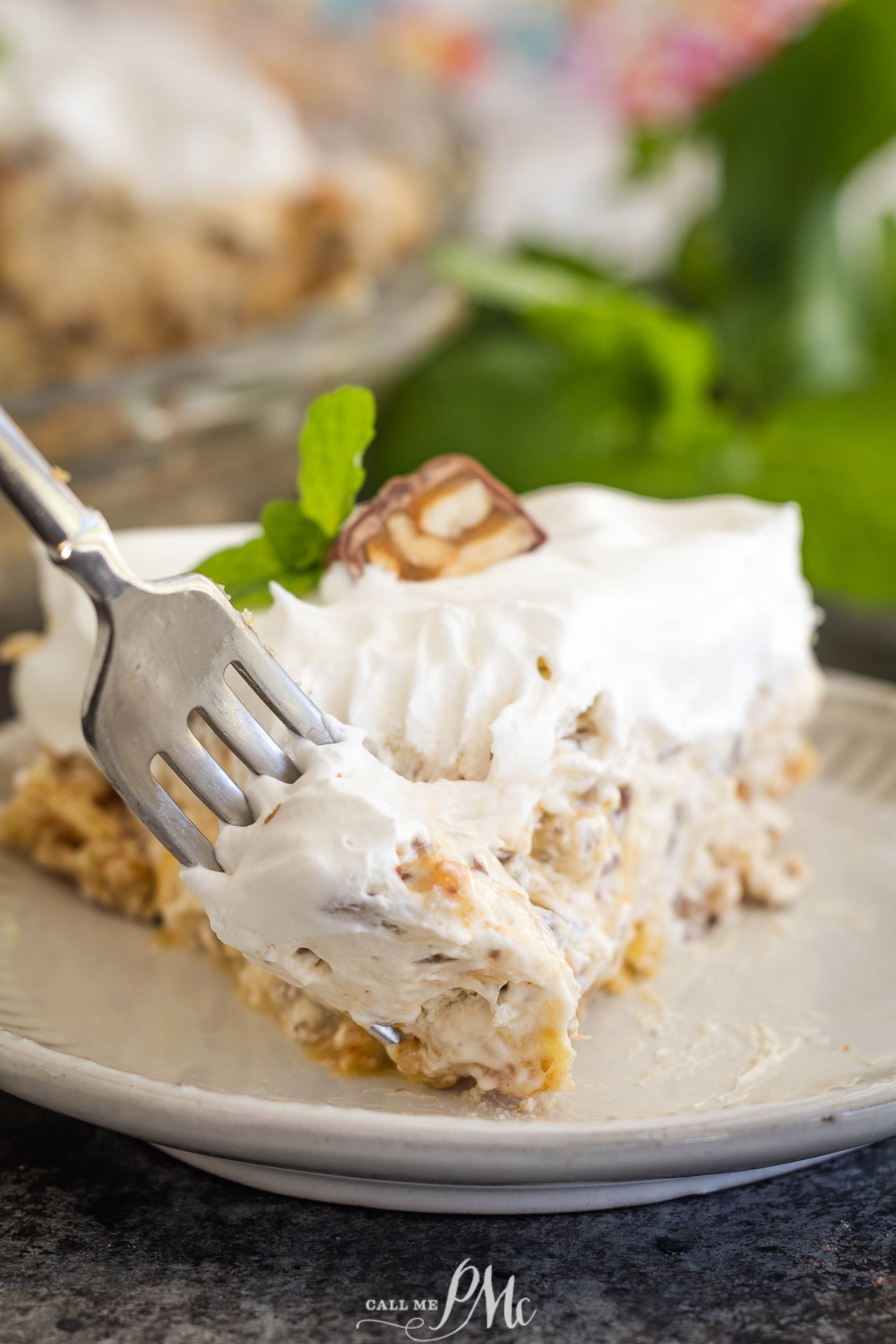 A fork slices into a creamy dessert reminiscent of a surprise million dollar pie, adorned with whipped cream and a chocolate piece. A mint leaf garnish completes the indulgence.