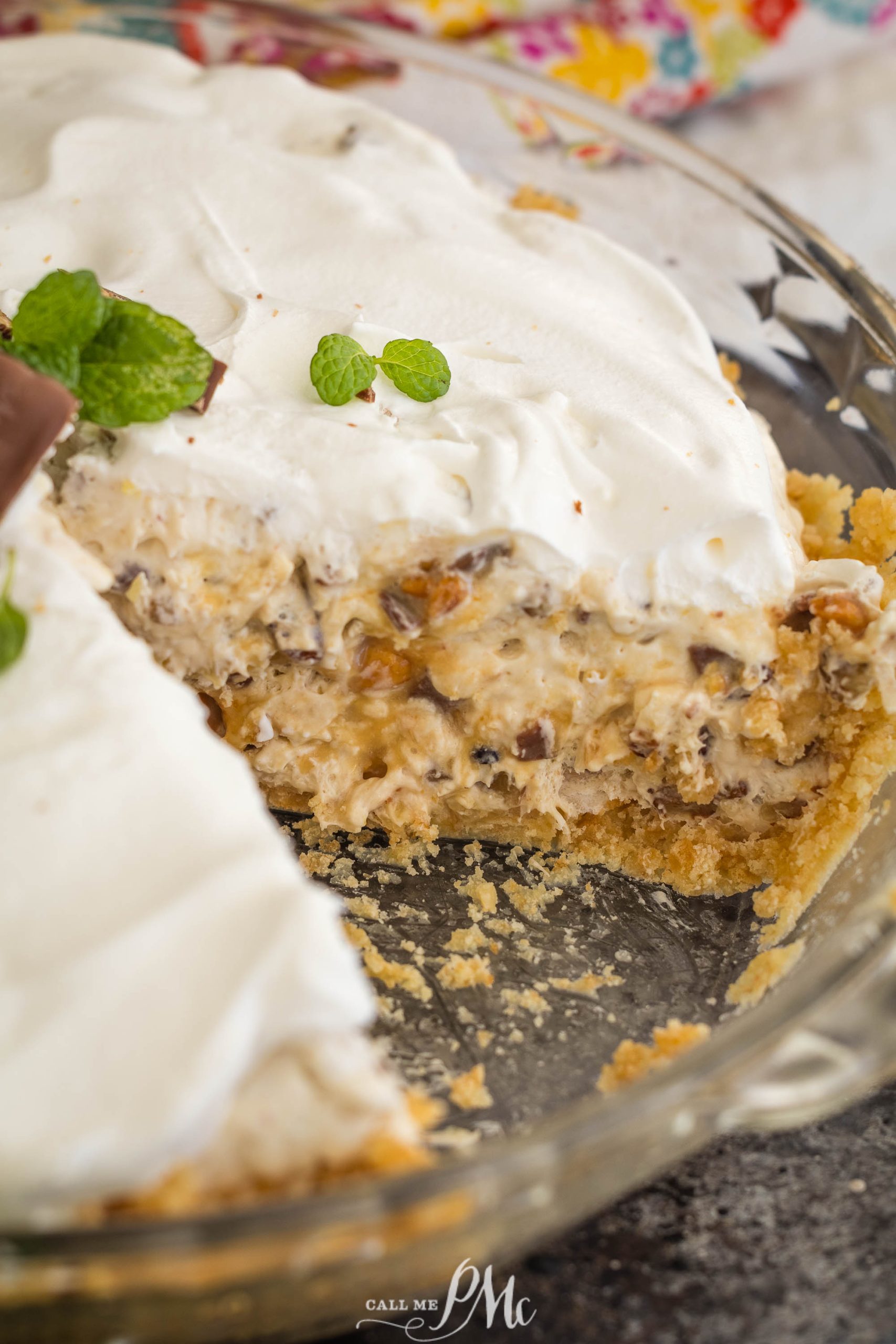 A slice of surprise million dollar pie reveals a creamy filling dotted with chocolate pieces, topped with white whipped cream and garnished with mint leaves, all nestled in a glass pie dish.