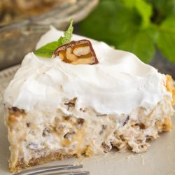 A slice of the surprisingly luscious million-dollar pie, topped with whipped cream and a small piece of chocolate, rests on a white plate with a fork nearby.