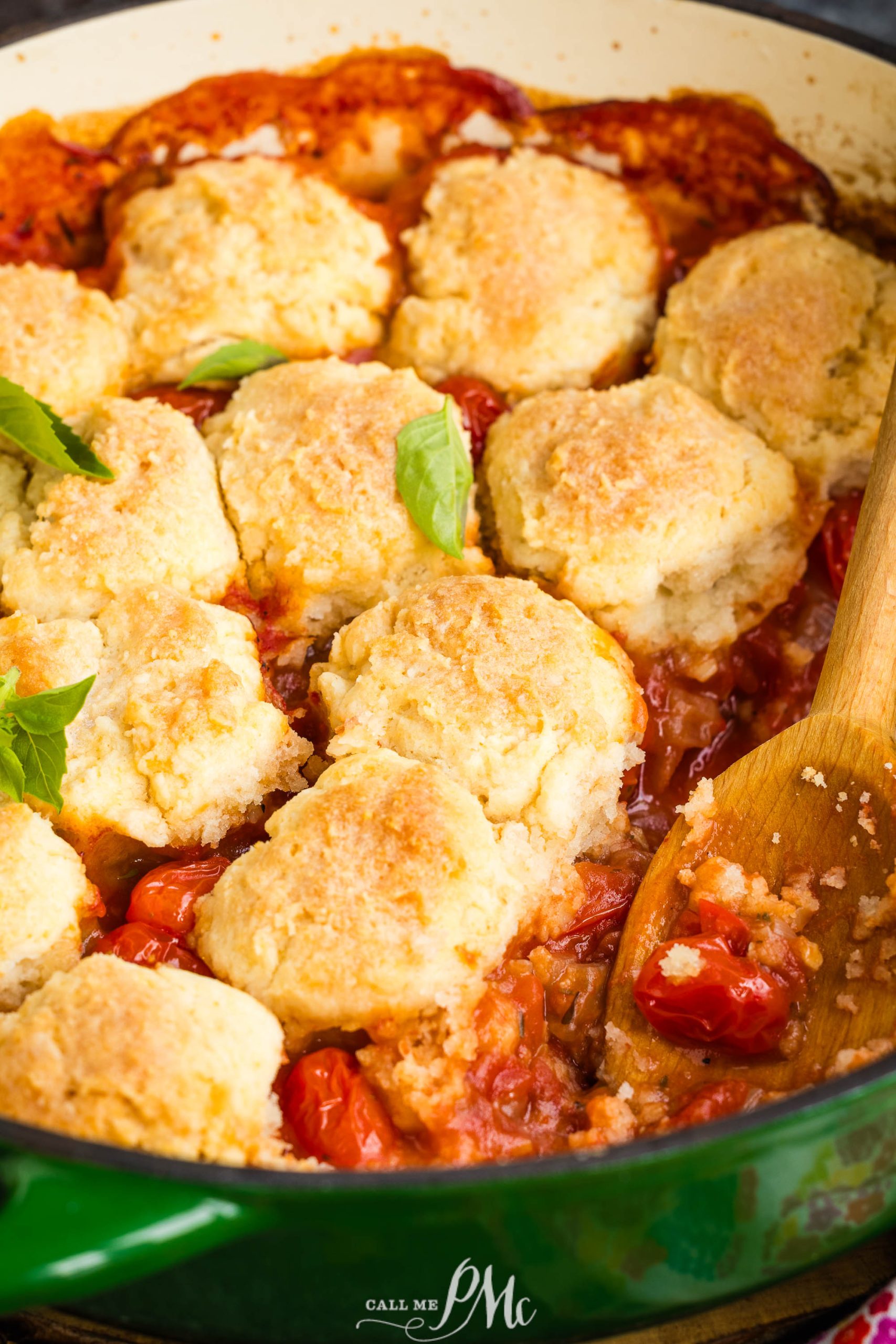 A baked dish with golden biscuits on top in a green casserole dish, garnished with fresh basil leaves.