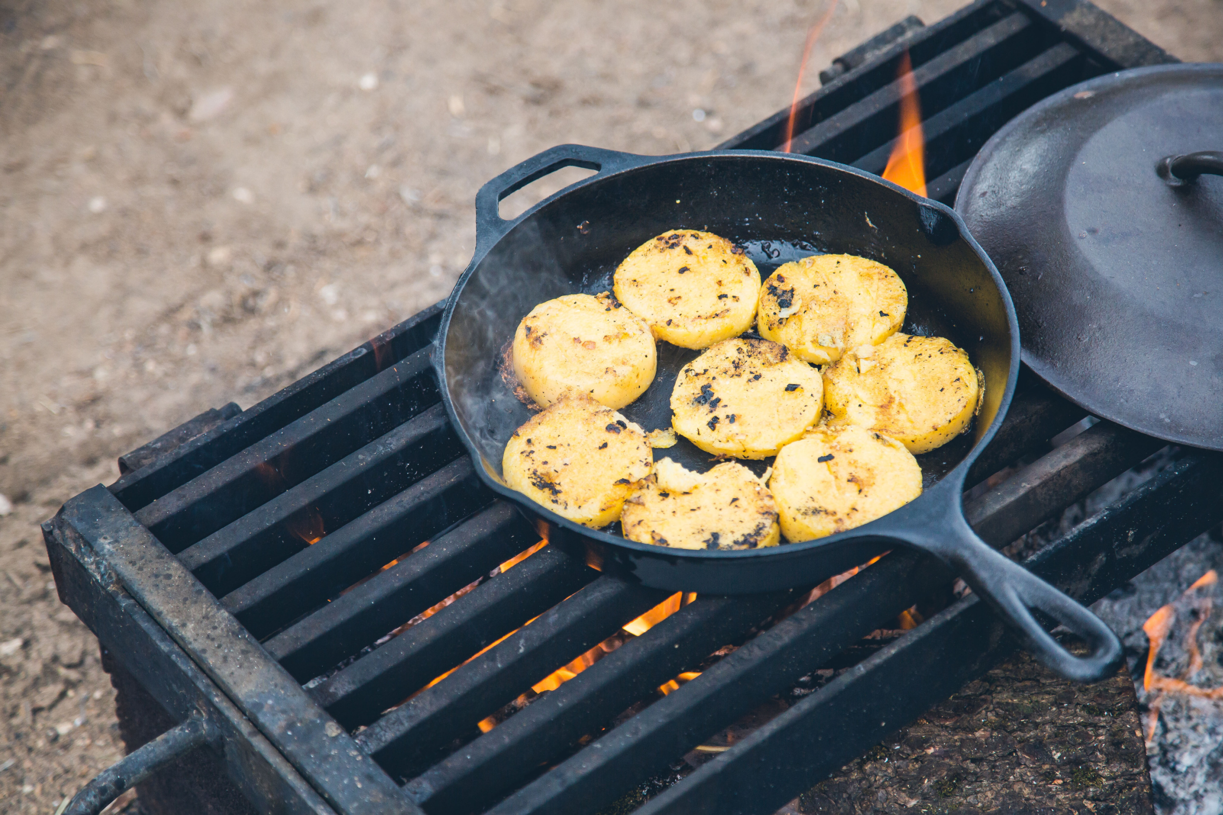 Corn cakes cooking on a cast iron skillet over an open fire grill outdoors.