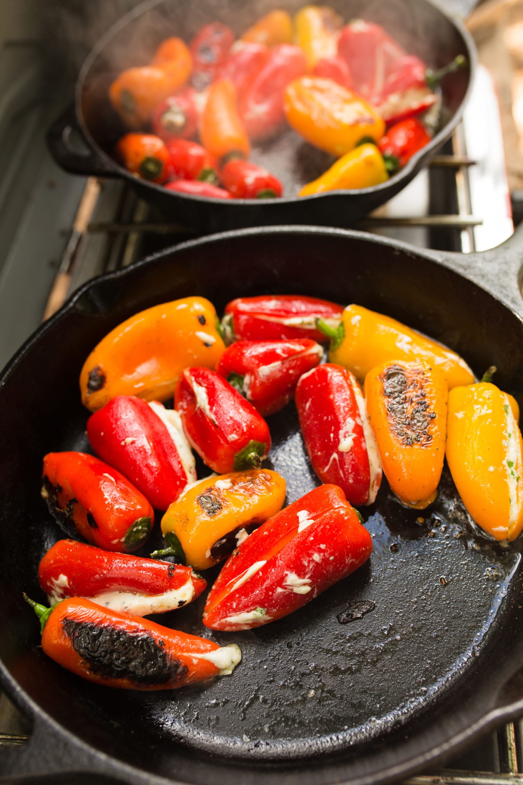 Red and yellow mini peppers being roasted in a pan on a stove.