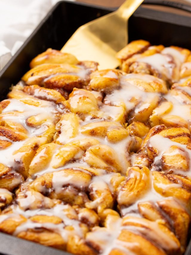 Golden brown cinnamon roll pull-apart bread in a rectangular pan, topped with white icing, with a gold spatula ready to serve.