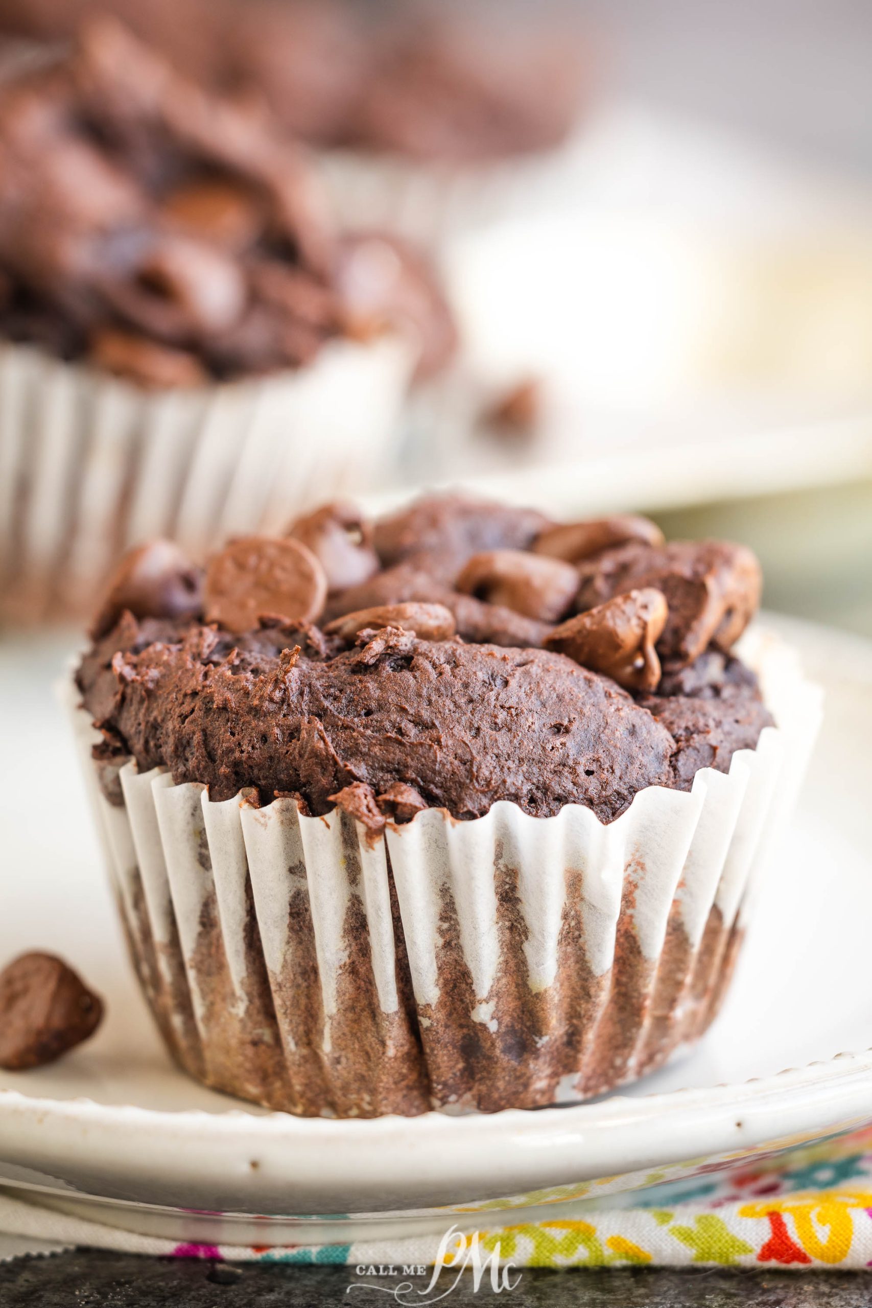 Chocolate muffin with chocolate chips on top, wrapped in a white paper liner.