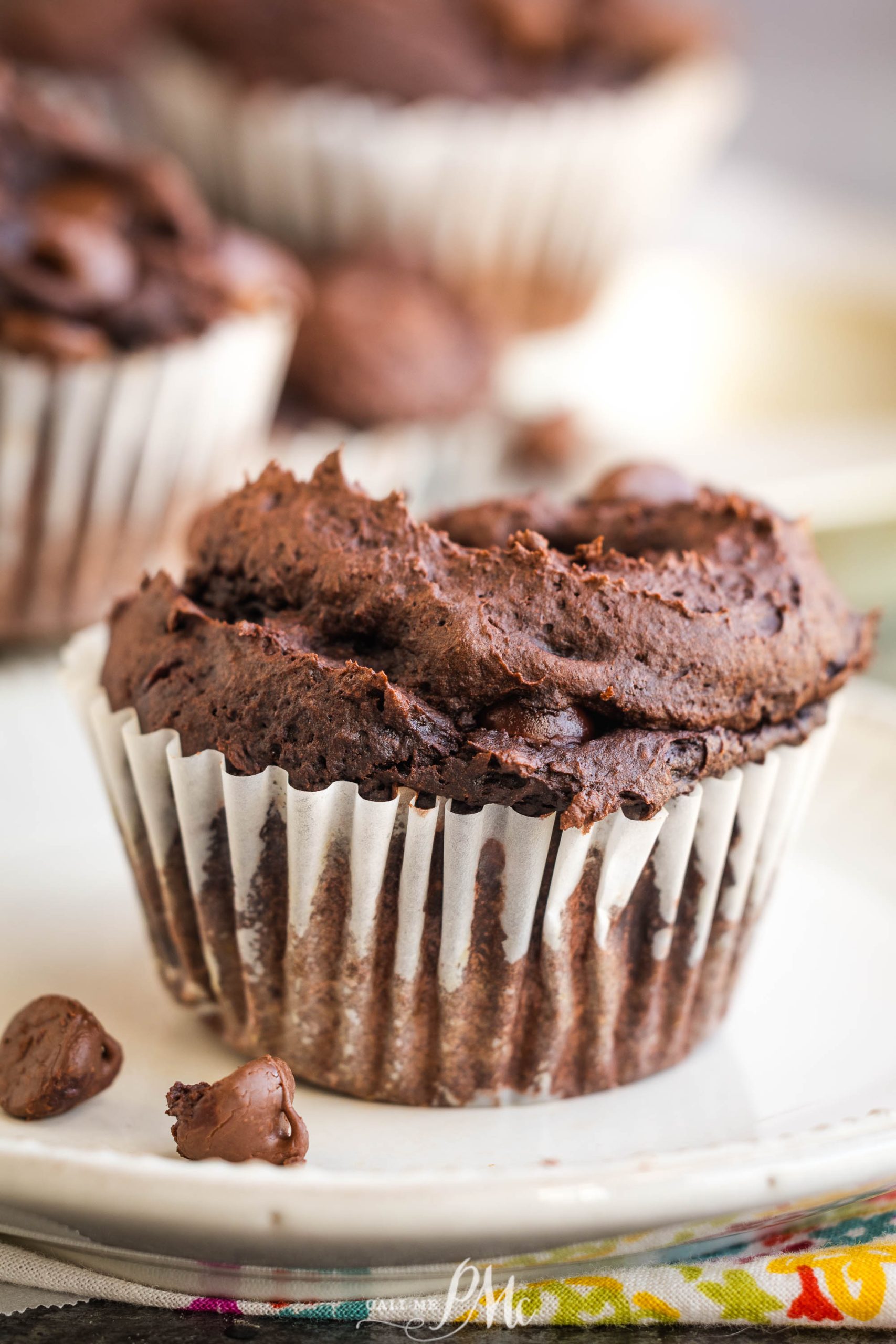 3 Ingredient Pumpkin Brownie Muffins in a white paper liner on a plate, with chocolate chips scattered nearby.