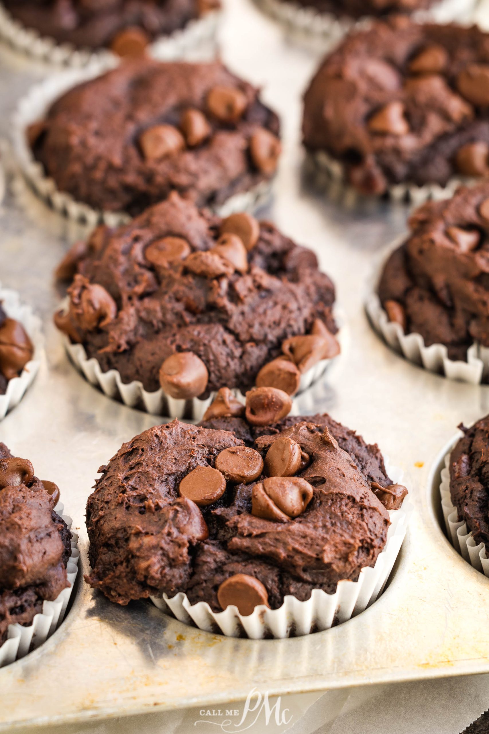 3 Ingredient Pumpkin Brownie Muffins with chocolate chips on top, arranged in individual white paper liners on a baking tray.