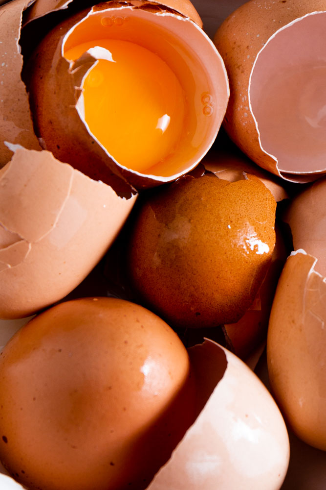 A close-up of several brown eggs, some cracked open to reveal yolks..