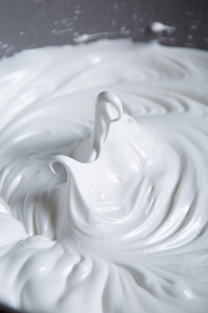 Close-up view of glossy, stiff peaks of meringue in a mixing bowl.