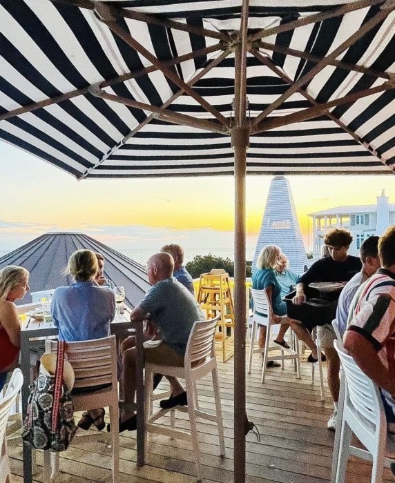 People dining outdoors under striped umbrellas at sunset.