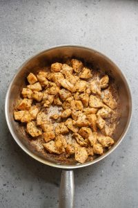 A skillet with cooked, seasoned chicken pieces on a gray countertop.