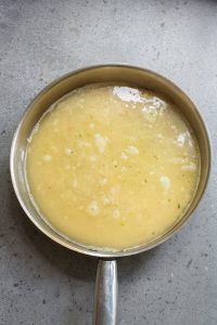 A saucepan filled with a creamy, light yellow soup resting on a gray countertop.