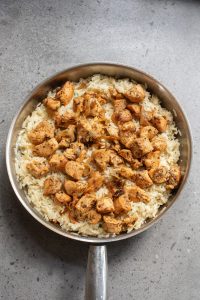 A skillet filled with cooked white rice topped with pieces of seasoned grilled chicken.