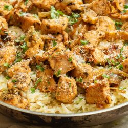 A skillet filled with seasoned chicken pieces and fluffy rice, garnished with chopped herbs.