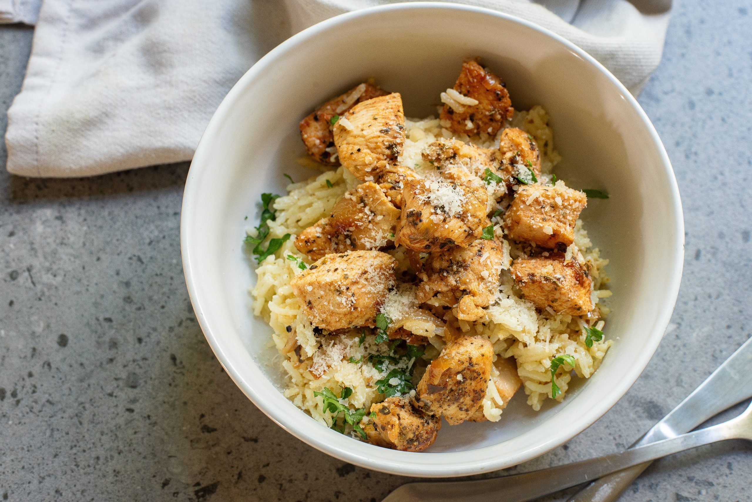 A bowl of food, garnished with herbs and grated cheese, on a textured surface.