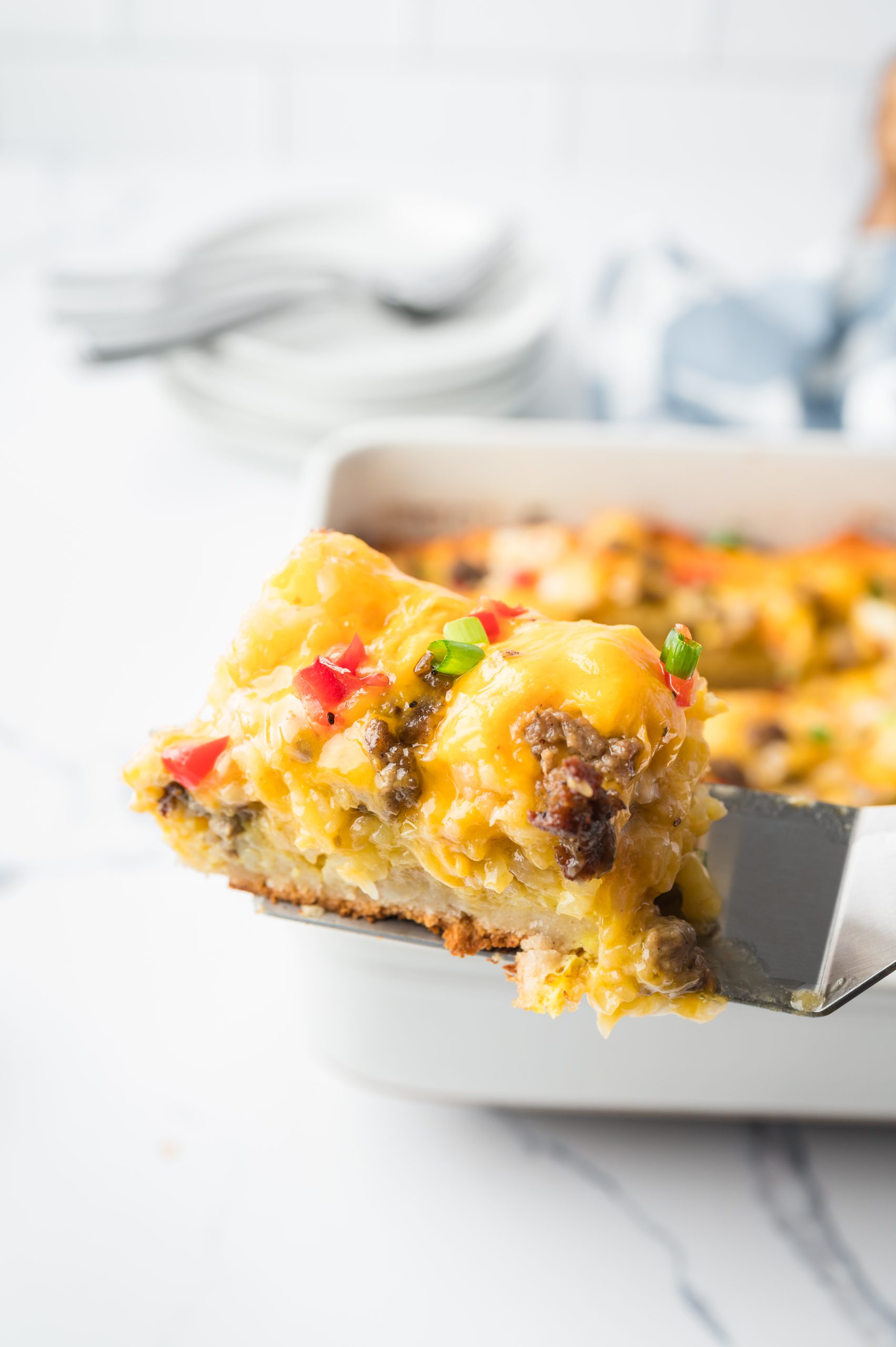 A serving of cheesy casserole with sausage, peppers, and a breadcrumb crust is lifted from a white baking dish.