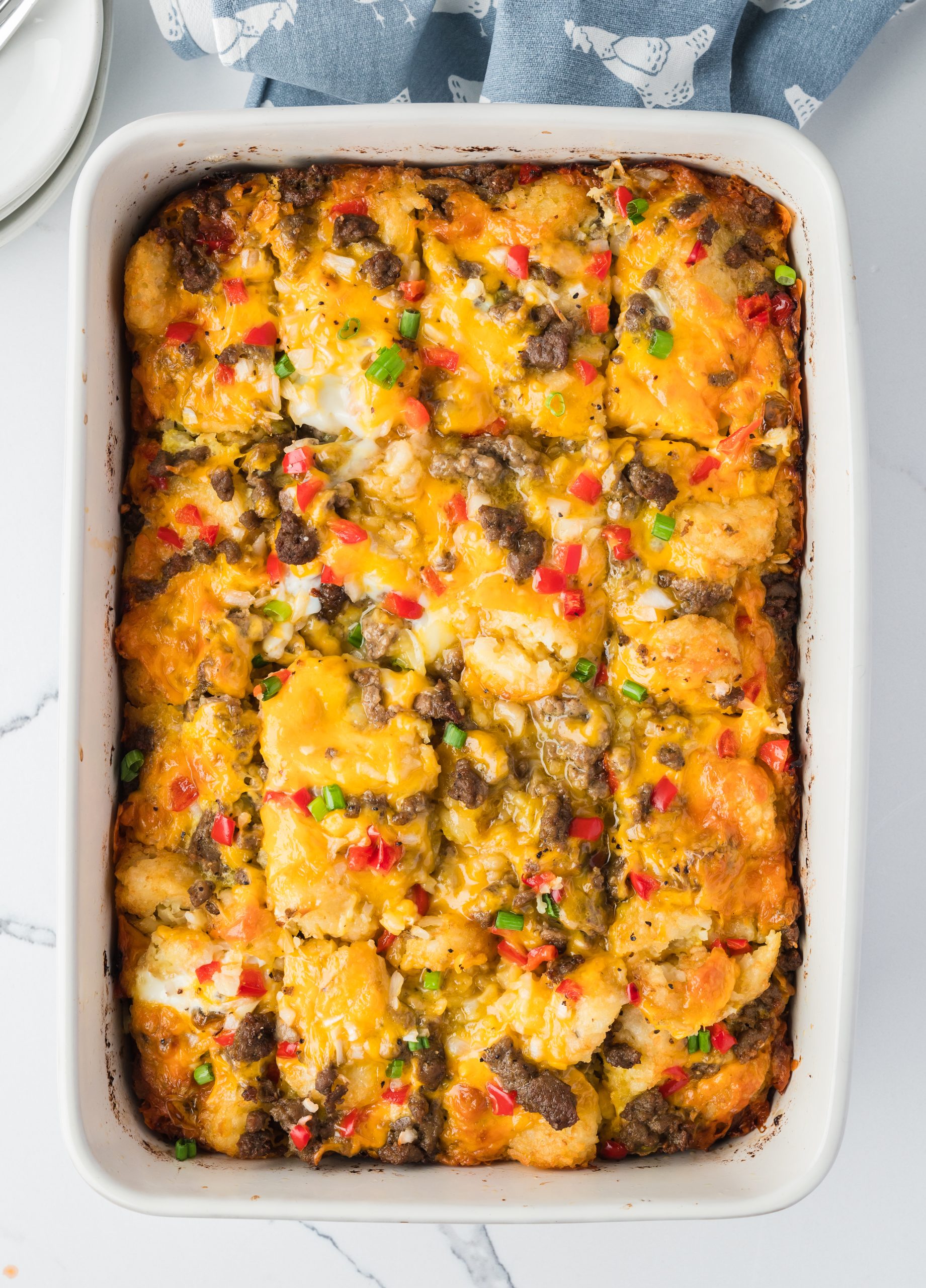 Baked casserole topped with melted cheese, ground beef, diced red and green peppers in a rectangular dish.