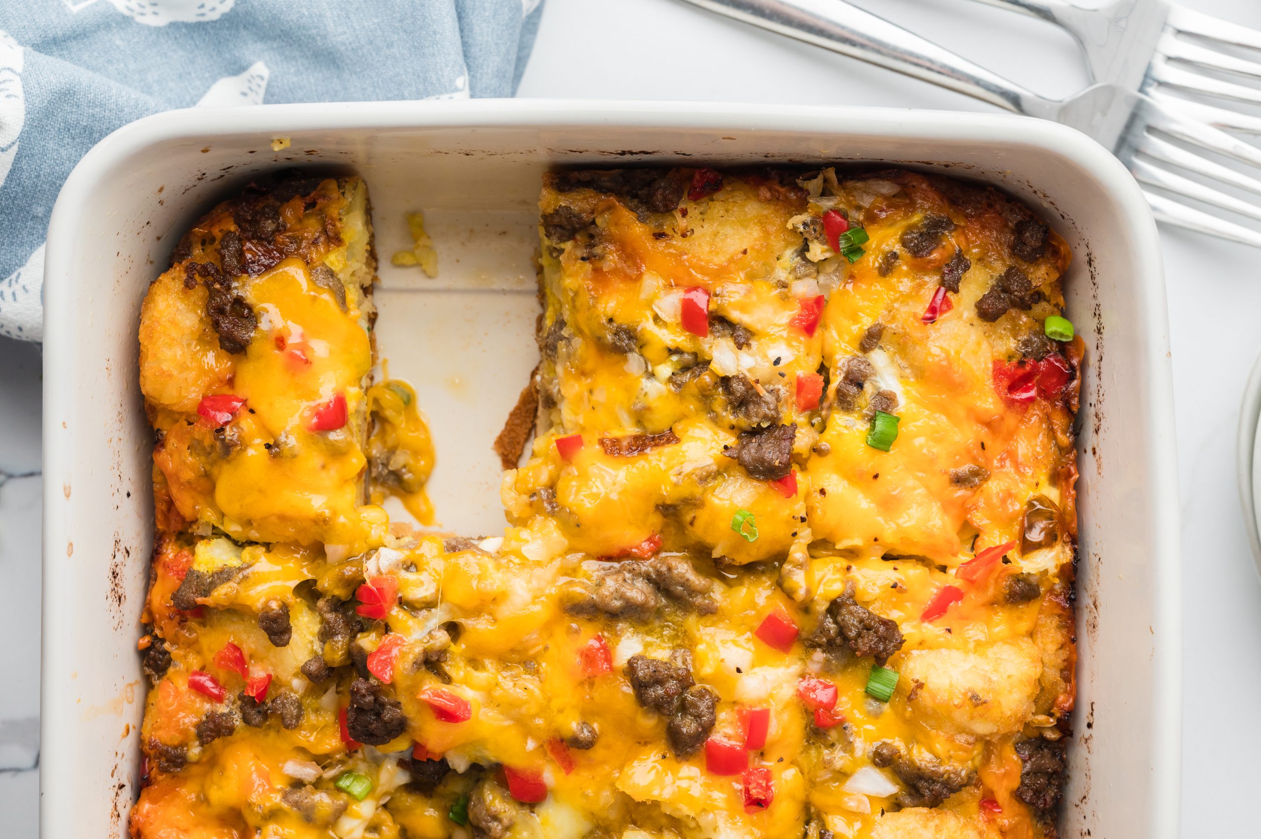 A baked casserole with melted cheese, ground meat, and diced red and green bell peppers, with a square slice missing from the corner.