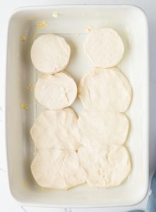 Unbaked biscuit dough rounds arranged in a rectangular baking dish.